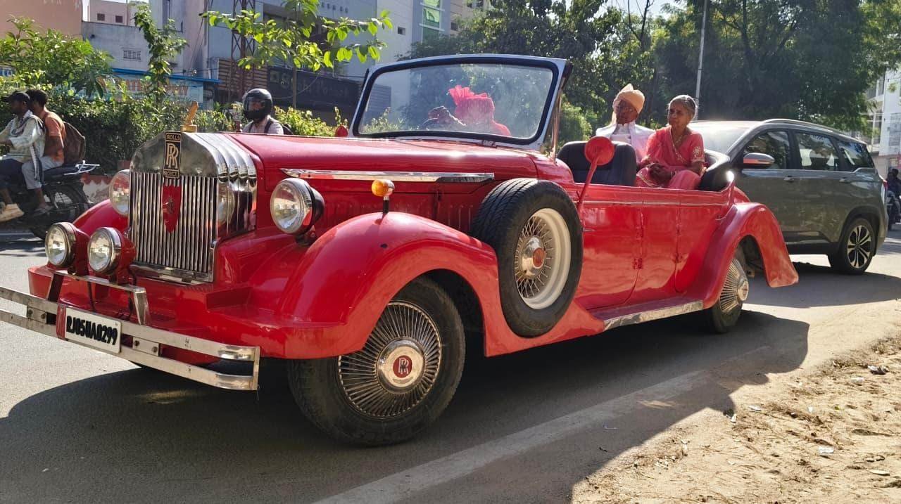 Couple riding in a red Rolls-Royce style vintage car for a wedding entry in Udaipur