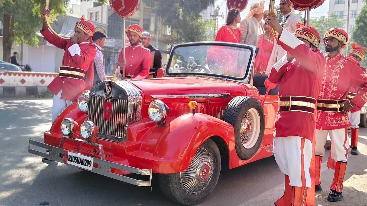 Baraat band beside a red Rolls-Royce style baraat vintage car in Udaipur