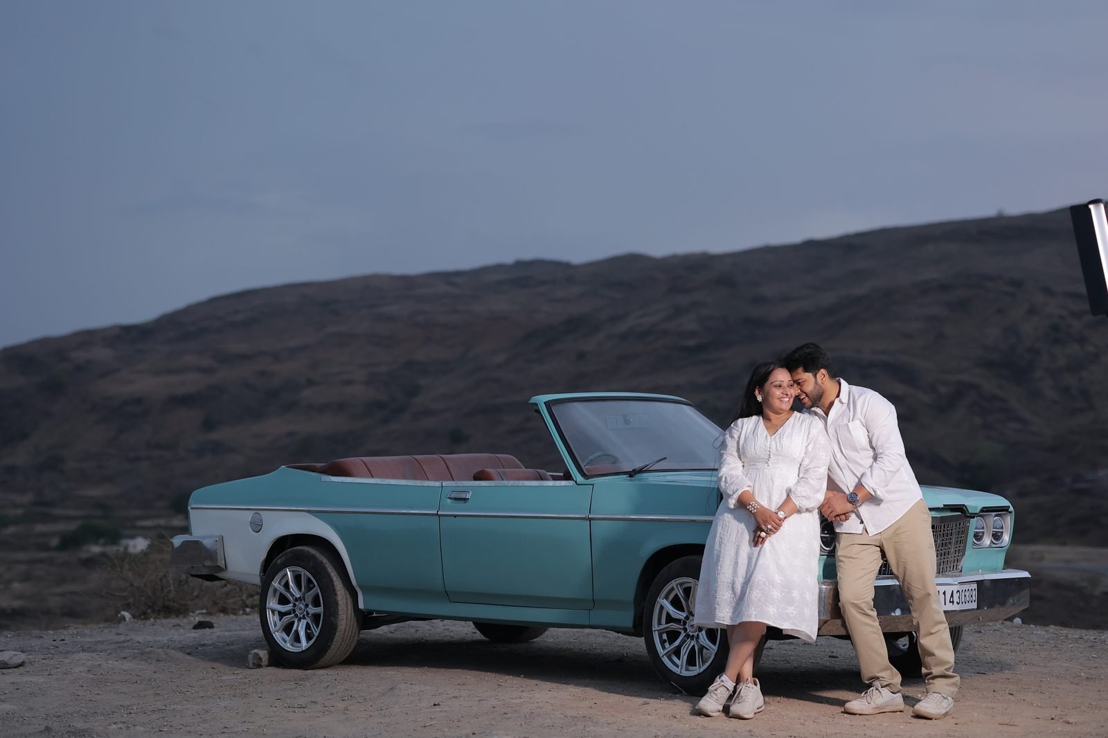 Couple leaning on a teal vintage convertible at dusk, prewedding car shoot in Udaipur