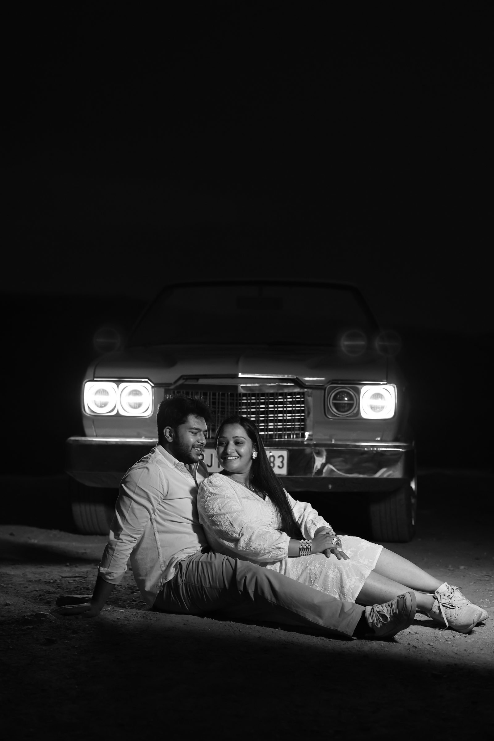 Black and white pre-wedding portrait of a couple with a vintage car's headlights on, Udaipur
