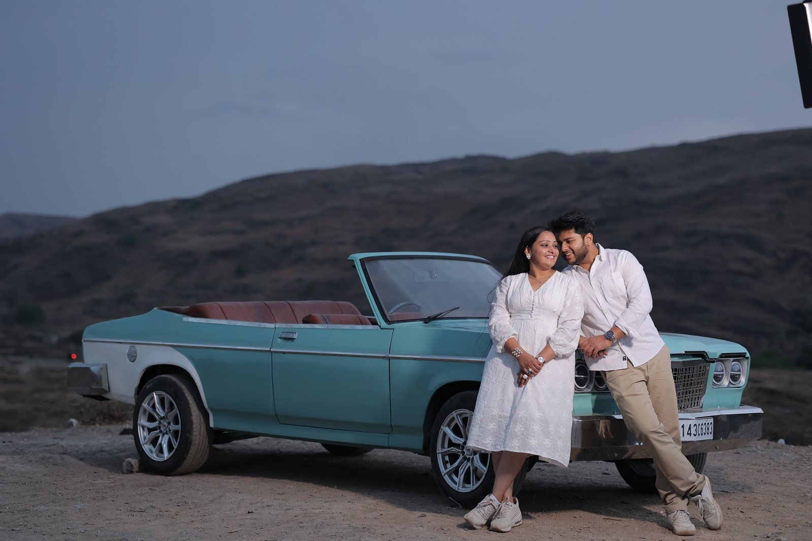 Couple posing with a teal vintage convertible for prewedding car booking in Udaipur